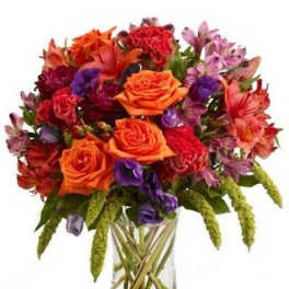 Vibrant bouquet of orange roses, red carnations and mixed blooms in a clear glass vase
