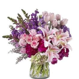 Mixed bouquet of pink lilies, roses, tulips, and purple flowers in a clear glass vase