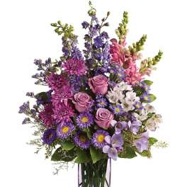 Tall arrangement of pink and purple flowers in a slender lavender glass vase
