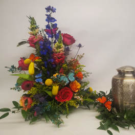 Tall mixed bouquet with roses, tulips, and butterflies beside a metal urn