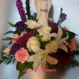 Floral arrangement with white lilies, roses, and purple blooms around an angel figurine