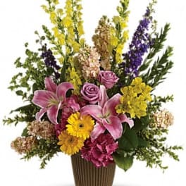 Mixed bouquet with pink lilies, roses, and yellow and purple spikes in a ribbed vase
