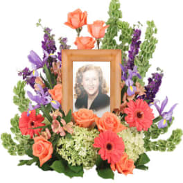 Framed portrait surrounded by orange roses, pink gerbera daisies, and purple flowers