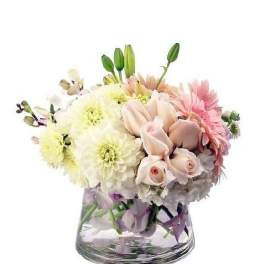 Low pastel arrangement of white dahlias, pink roses, and gerbera daisies in a clear glass vase