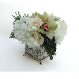 Low white and green floral arrangement with orchids in an ornate silver cube vase