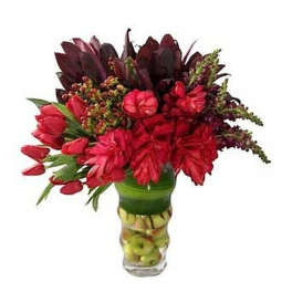 Tall arrangement of red flowers in a clear vase filled with stacked green apples