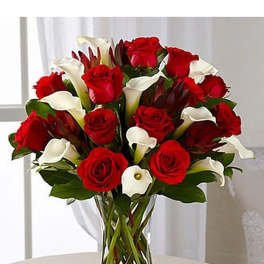 Arrangement of red roses and white calla lilies in a clear glass vase on a light table