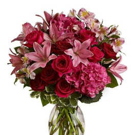 Arrangement of red roses, pink lilies, hydrangeas, and alstroemeria in a clear glass vase