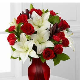 Arrangement of white lilies, red roses, and red carnations in a red glass vase.