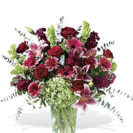 Tall arrangement of red roses, pink lilies, gerbera daisies, and green hydrangea in a clear glass vase