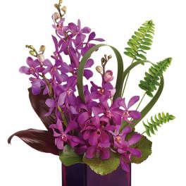Tall purple orchid arrangement with curled foliage and ferns in a purple glass cube vase