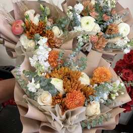 Three wrapped bouquets with orange, white, and cream flowers