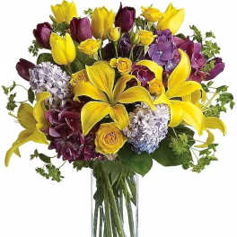 Bouquet of yellow lilies, purple tulips, and hydrangeas in a clear glass vase