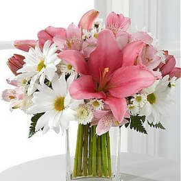 Pink lilies and white daisies arranged in a clear rectangular glass vase