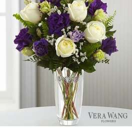 Arrangement of white roses and purple lisianthus in a clear glass vase with a jeweled band.