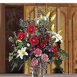 Tall mixed arrangement of red, white, yellow, and purple flowers in a cut-glass vase on a pedestal.