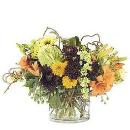 Low arrangement of orange lilies, yellow and dark blooms with green accents in a clear glass vase