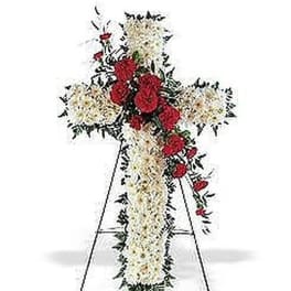 Standing cross of white flowers with red roses on a metal easel.