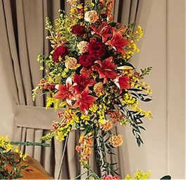 Tall standing spray of red lilies and roses with yellow and peach flowers on an easel indoors