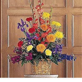 Tall mixed arrangement of red, yellow, orange, and purple flowers in a wicker basket