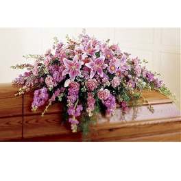 Pink and lavender casket spray with lilies, carnations, and daisies on a wooden casket