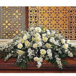 Large white and cream floral casket spray arranged across a wooden casket
