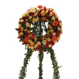 Standing wreath of red, orange, and yellow roses on a greenery-covered tripod easel