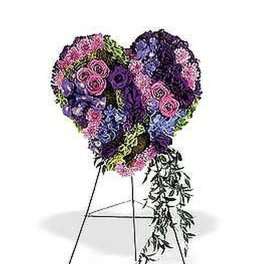 Heart-shaped standing floral spray in purple, pink, and lavender tones on a metal easel.
