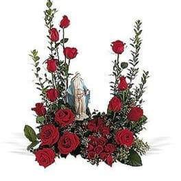 Red rose arrangement with tall greenery framing a religious figurine in the center.