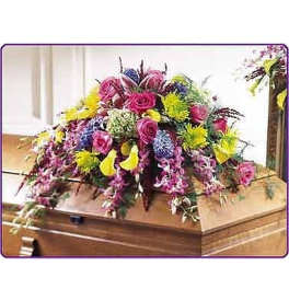 Colorful casket spray with pink roses, yellow mums, and trailing purple flowers on a wooden casket