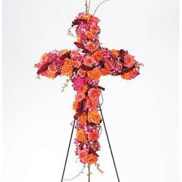 Tall cross-shaped funeral spray of orange and pink roses on a metal easel stand