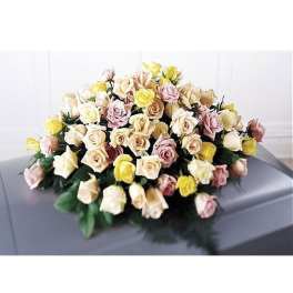Pastel yellow, cream, and pink roses arranged as a casket spray on a gray casket