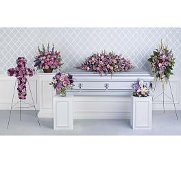 Set of pink and purple funeral floral arrangements around a silver casket.