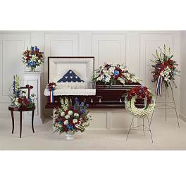 Patriotic funeral floral set with red, white, and blue arrangements around a casket and wreath on a stand
