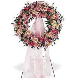 Pink and peach floral wreath with long pink ribbon displayed on a metal easel stand