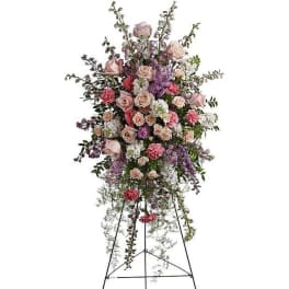 Tall pastel standing spray of roses, carnations, and mixed flowers on a black metal easel