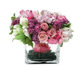 Low pink and purple flower arrangement in a clear square vase with black stones