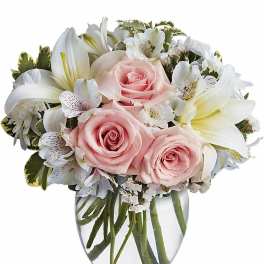 Round arrangement of pale pink roses and white lilies in a clear glass vase