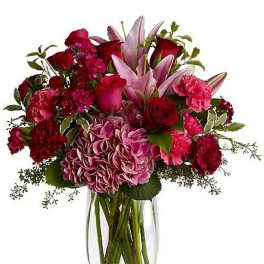 Mixed arrangement of pink lilies, roses, carnations, and hydrangea in a clear glass vase