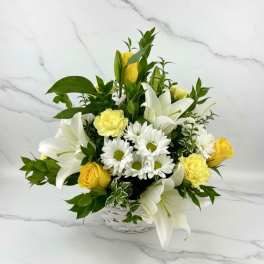 White lilies, yellow roses, and white daisies in a white basket