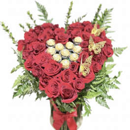 Heart-shaped bouquet of red roses with chocolates and butterfly accents in a vase