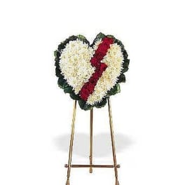Heart-shaped white floral standing spray with red diagonal stripe on a metal easel