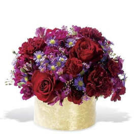 Low arrangement of red roses, red carnations, and purple asters in a cream round box