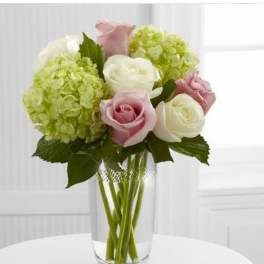 Arrangement of pale pink roses, white roses, and green hydrangeas in a clear glass vase