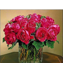 Compact arrangement of hot pink roses in a clear glass cube vase on a wooden table