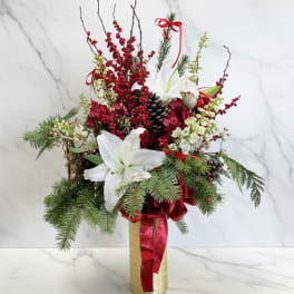 Holiday arrangement with white lilies, red berries, and pine in a gold vase