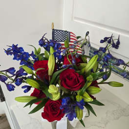 Red roses and blue flowers in a clear vase with an American flag