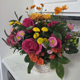 Mixed bouquet of pink roses, yellow mums, and orange flowers in a white basket