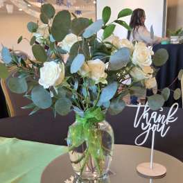 White roses in a clear glass vase with eucalyptus and a green ribbon