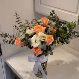 Peach and white roses arranged in a clear glass vase with a ribbon.